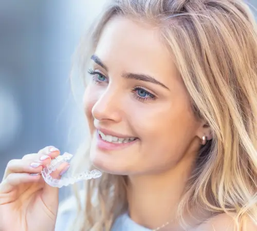 Smiling woman placing a clear aligner on her teeth