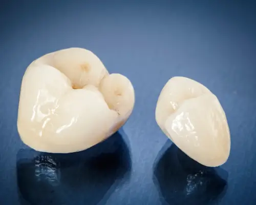 Two ceramic dental crowns on a dark blue surface