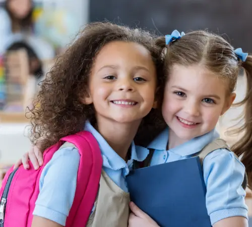 Two smiling schoolgirls in uniforms hugging